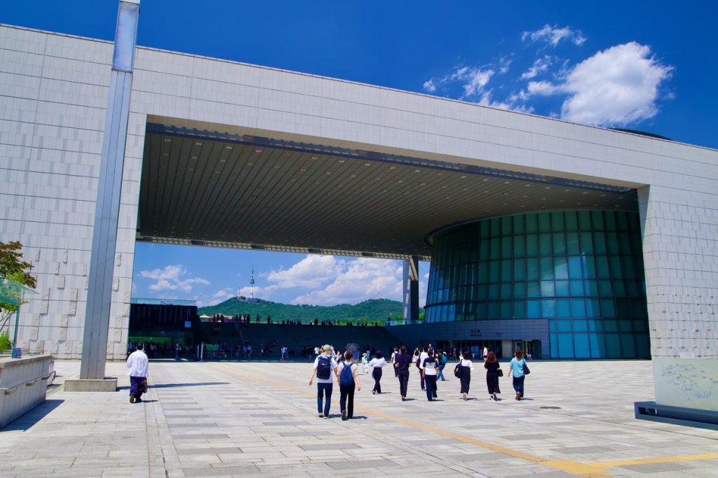 A wide-angle view captures the impressive front facade of the National Museum of Korea, highlighting its distinctive square opening, a modern architectural marvel amidst Seoul's skyline.